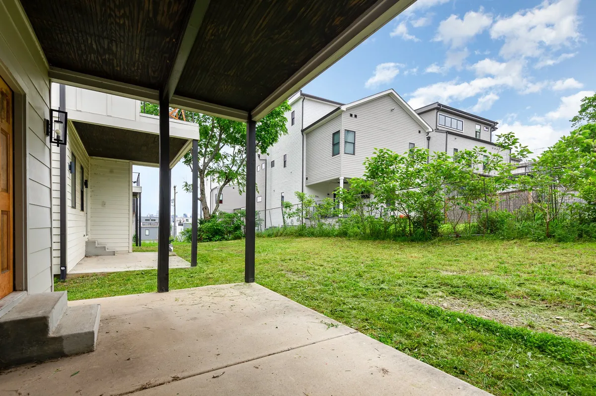 A tranquil exterior view of a patio area surrounded by lush greenery and neighboring houses. The setup is ideal for outdoor gatherings, relaxation, and enjoying the fresh air just outside the main living spaces.