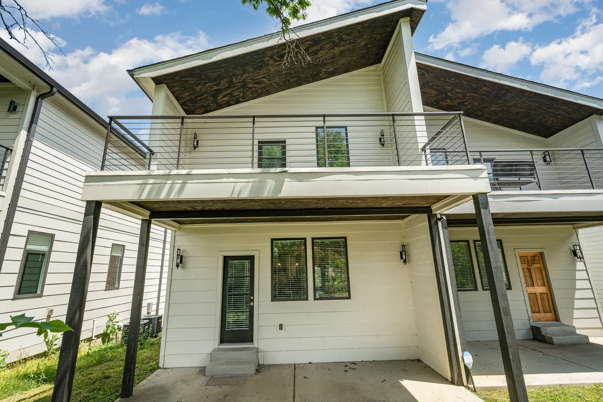An exterior view of a modern home featuring a welcoming balcony and front door, with ample space for gatherings or enjoying the fresh air. The modern architecture and open balcony hint at communal experiences while also allowing for quiet retreat.