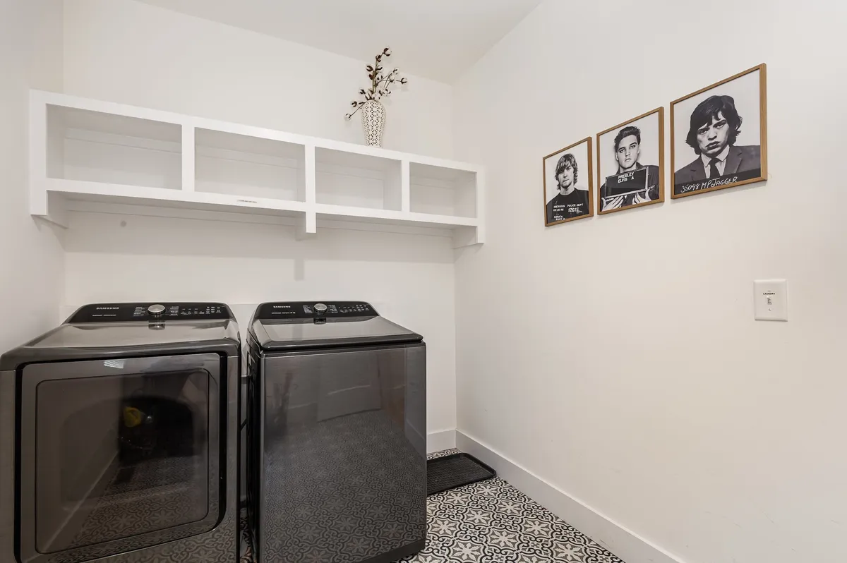 This interior image highlights a modern laundry room with washing machines, framed portraits, and a decorative vase. The setup conveys convenience and style, with enough space for laundry needs in each unit.