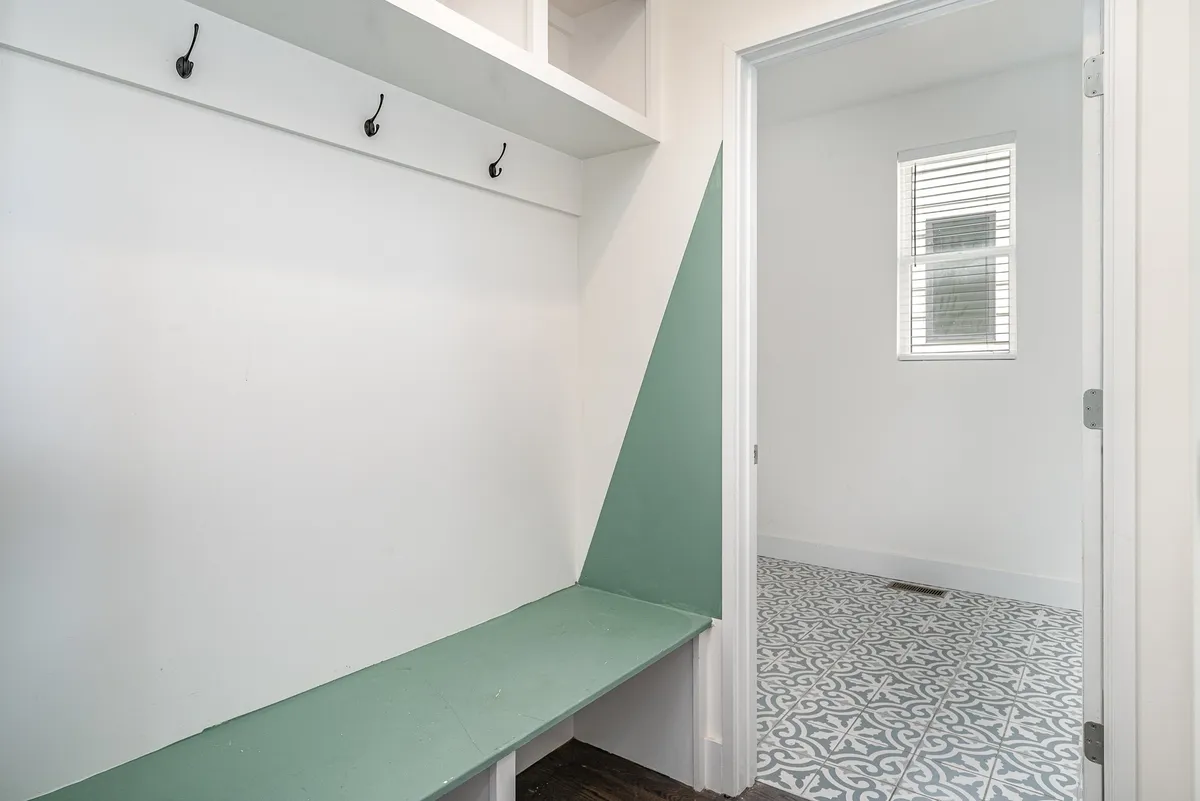A functional entryway space featuring bench seating, a green accent wall, and hooks for coats, highlighting organized daily living and a welcoming transition from outside to inside.