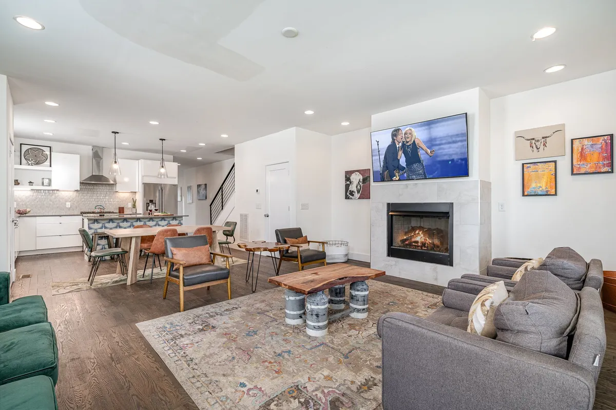 A cozy, contemporary living room featuring a fireplace, large television, ample seating around a coffee table, and a stylish area rug. The arrangement is inviting and perfect for group gatherings, movie nights, and casual conversations.