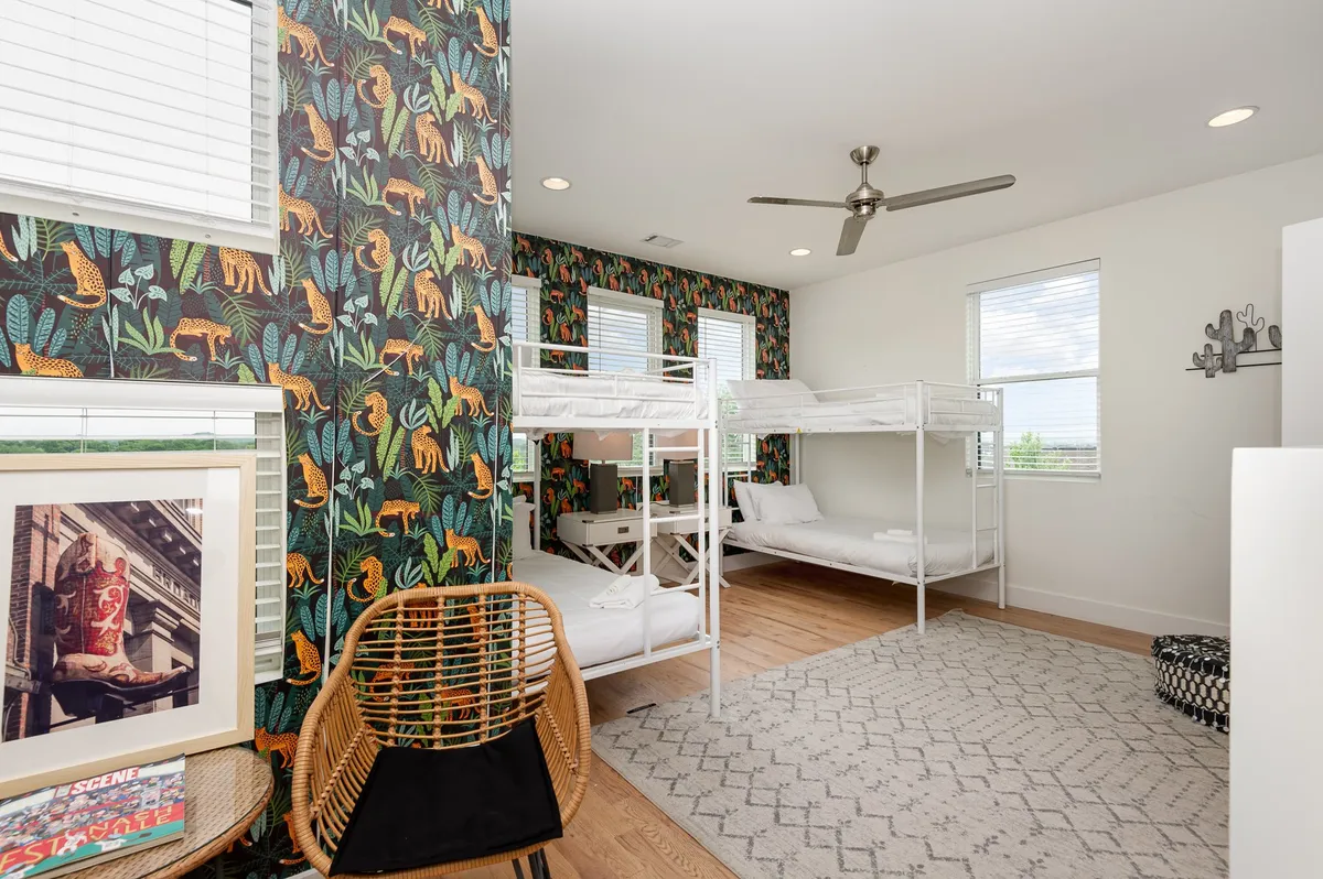 A cheerful and bright bunk room with multiple bunk beds, lively tropical wallpaper, a woven chair, and a patterned rug. The vibrant decor and ample natural light make it perfect for kids or friends sharing fun-filled sleepovers.