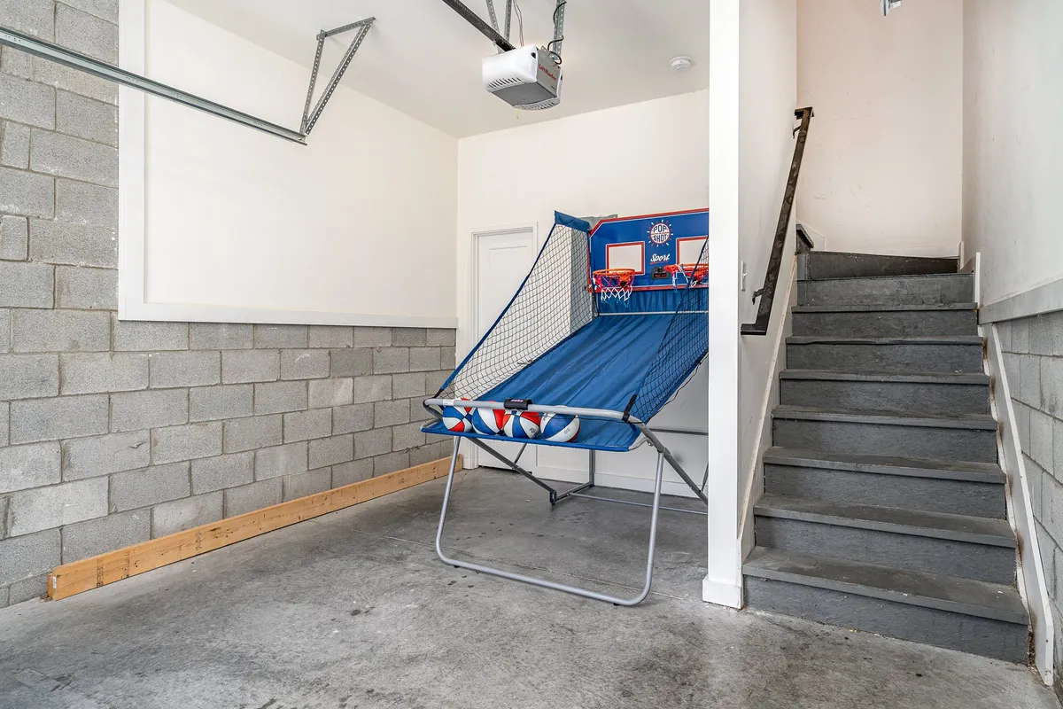 A vibrant, fun interior scene showcasing a basketball arcade game near a staircase and garage walls. The atmosphere is energetic, inviting friendly competition and shared laughter.