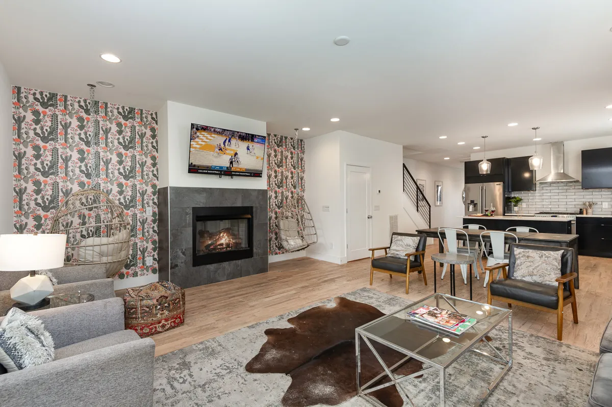 The image showcases an inviting living area with a modern fireplace as the centerpiece, stylish hanging chairs, a large TV perfect for game days, and a spacious dining area ready for group meals. The space feels both cozy and energetic, blending comfort and style for gatherings and relaxation.