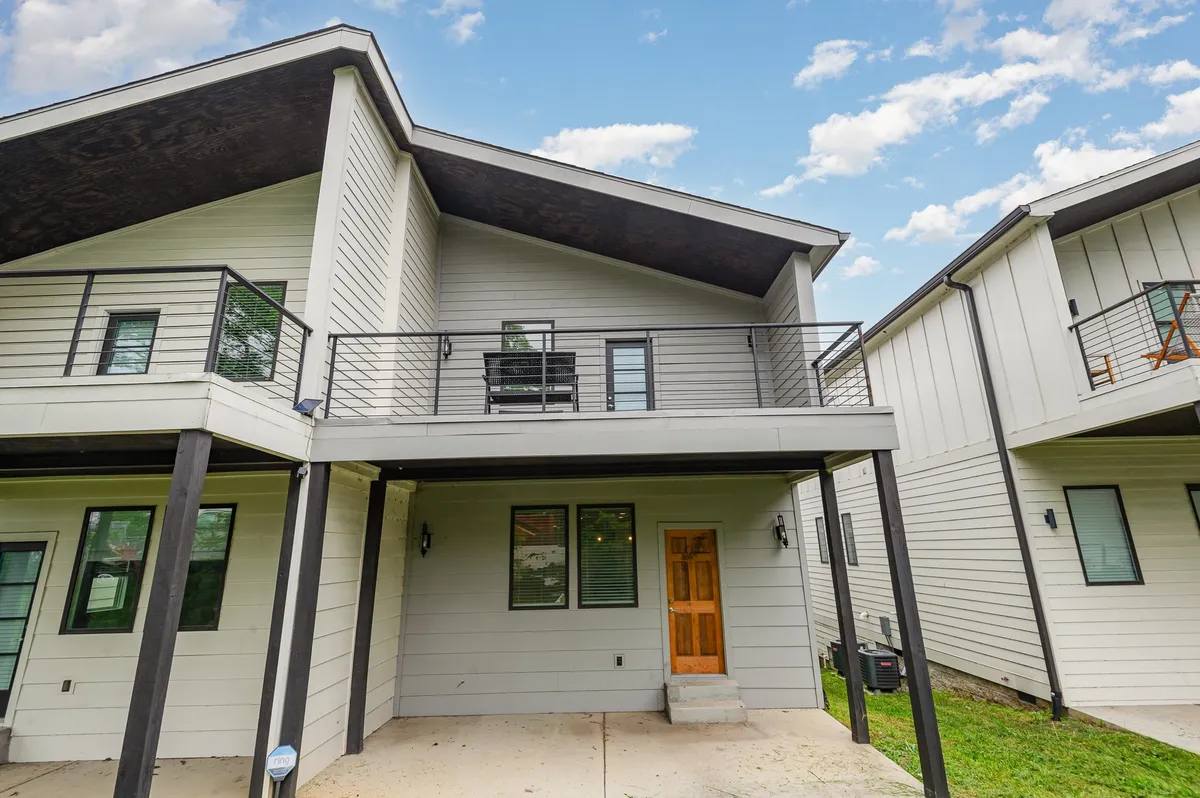 An exterior view of a two-story modern home featuring a balcony with seating and a welcoming front door, set against a manicured green lawn. The outdoor balcony area hints at private moments of relaxation with beautiful views.