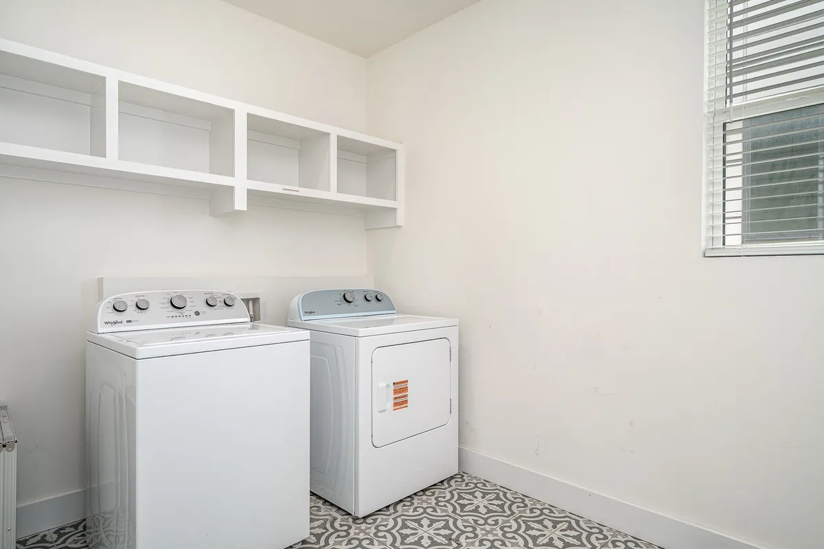 A tidy and well-organized laundry area with a washer, dryer, and shelves for storage, conveying a functional and practical space ideal for group stays.